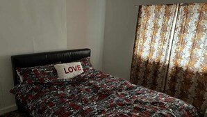 Un dormitorio con una cama, un almohadón con la palabra 'LOVE' y una cortina estampada con motivos florales.