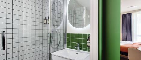 Un baño moderno con cabina de ducha de vidrio, un lavabo blanco y una pared revestida de azulejos verdes.