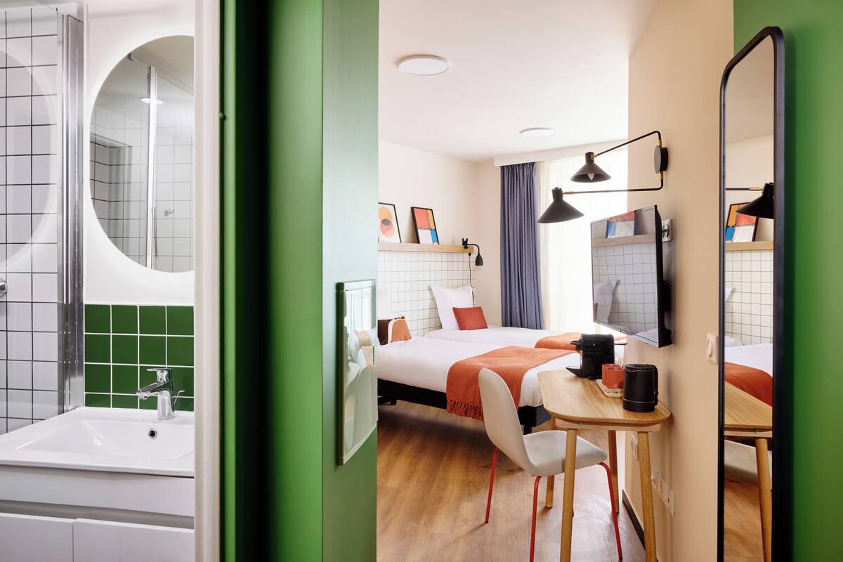 A hotel room with a shower, a bed with a TV, a desk, and a chair.