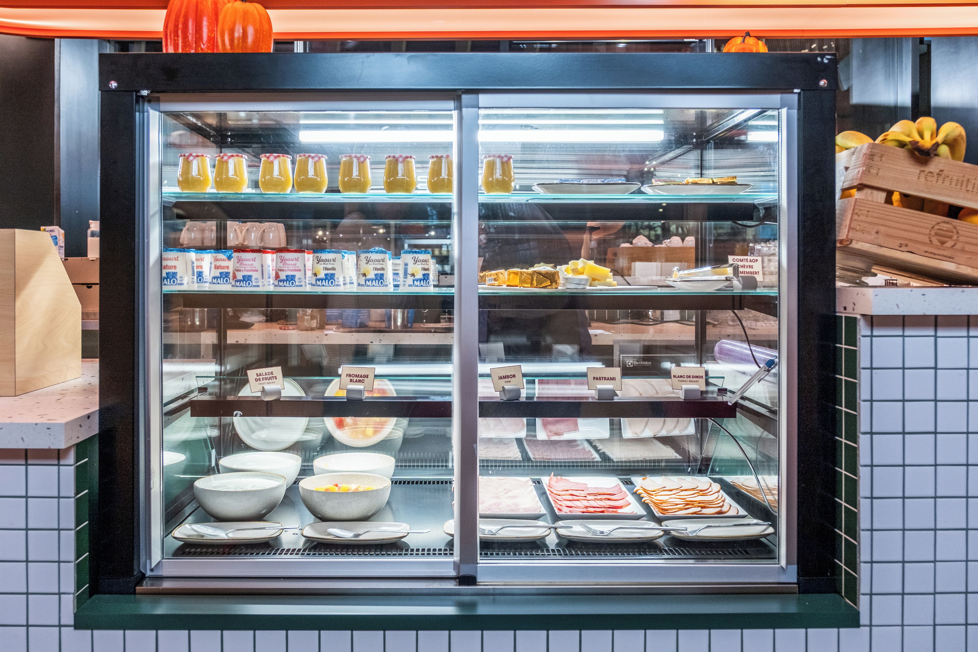 Un présentoir réfrigéré contenant divers produits alimentaires, notamment des yaourts, des salades de fruits et de la charcuterie.