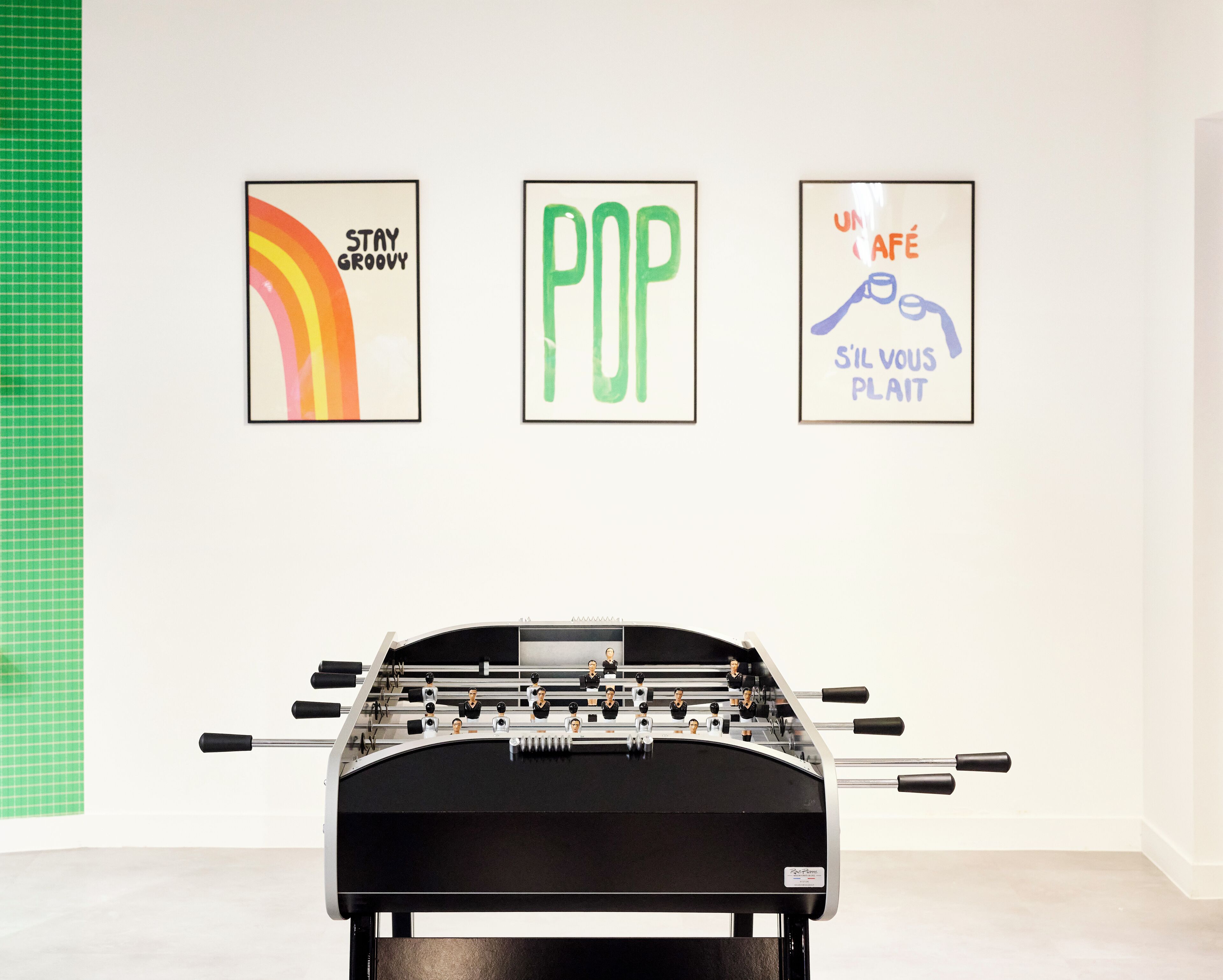 Una mesa de fútbol de mesa en una habitación con tres carteles enmarcados en la pared.