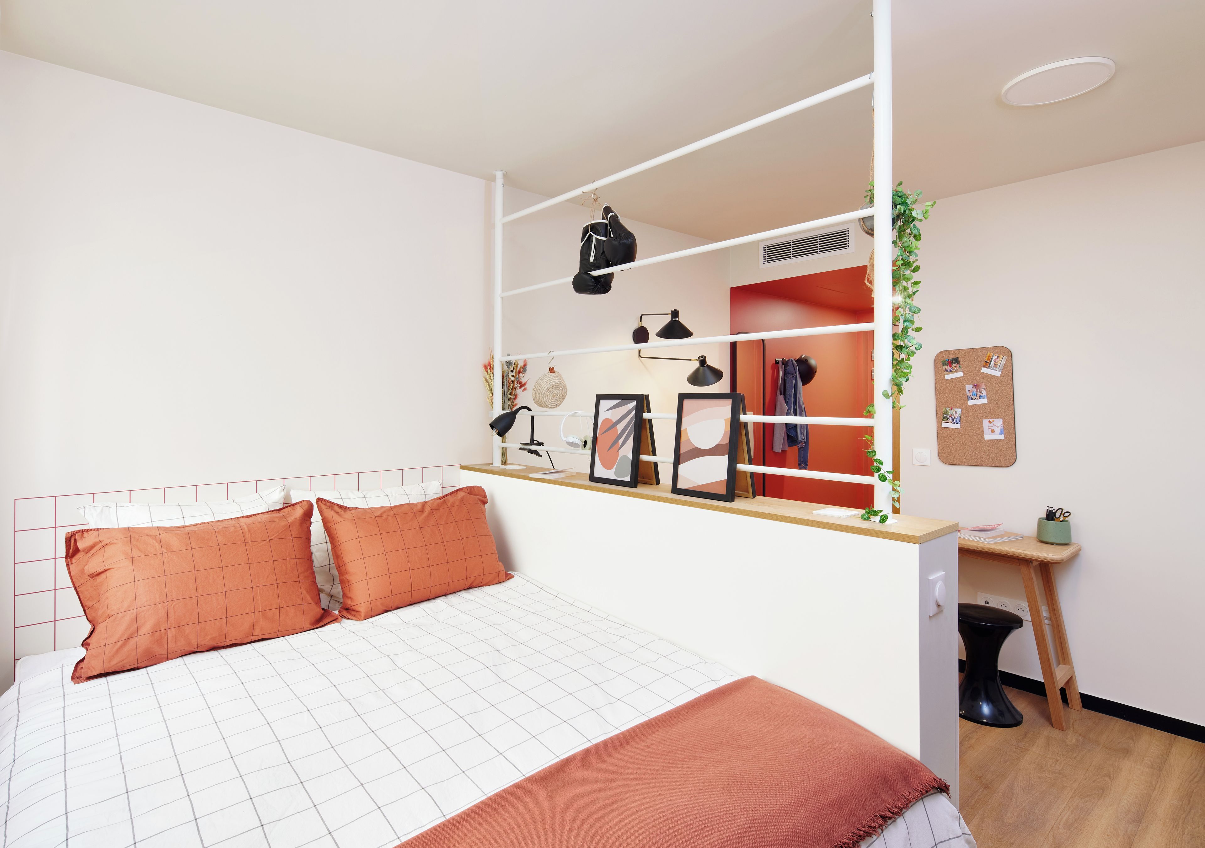 A bedroom with a bed, a desk, a wardrobe, and a corkboard on the wall.