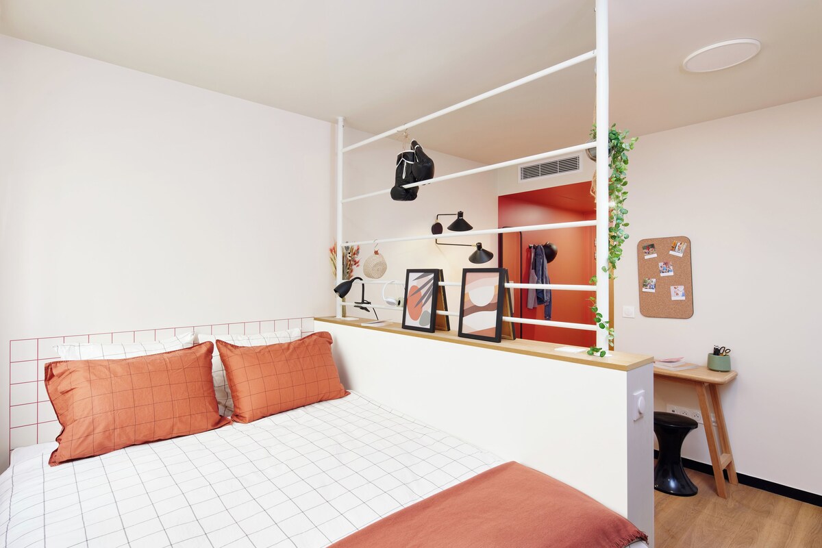 Ein Schlafzimmer mit Bett, Schreibtisch, Kleiderschrank und einer Pinnwand.