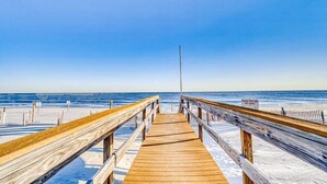 Un paseo marítimo de madera que conduce a una playa, con un letrero que advierte sobre el peligro de caminar sobre las dunas.