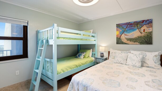 Une chambre avec un lit superposé, un lit simple, une fenêtre, un tableau et une table de chevet avec une lampe.