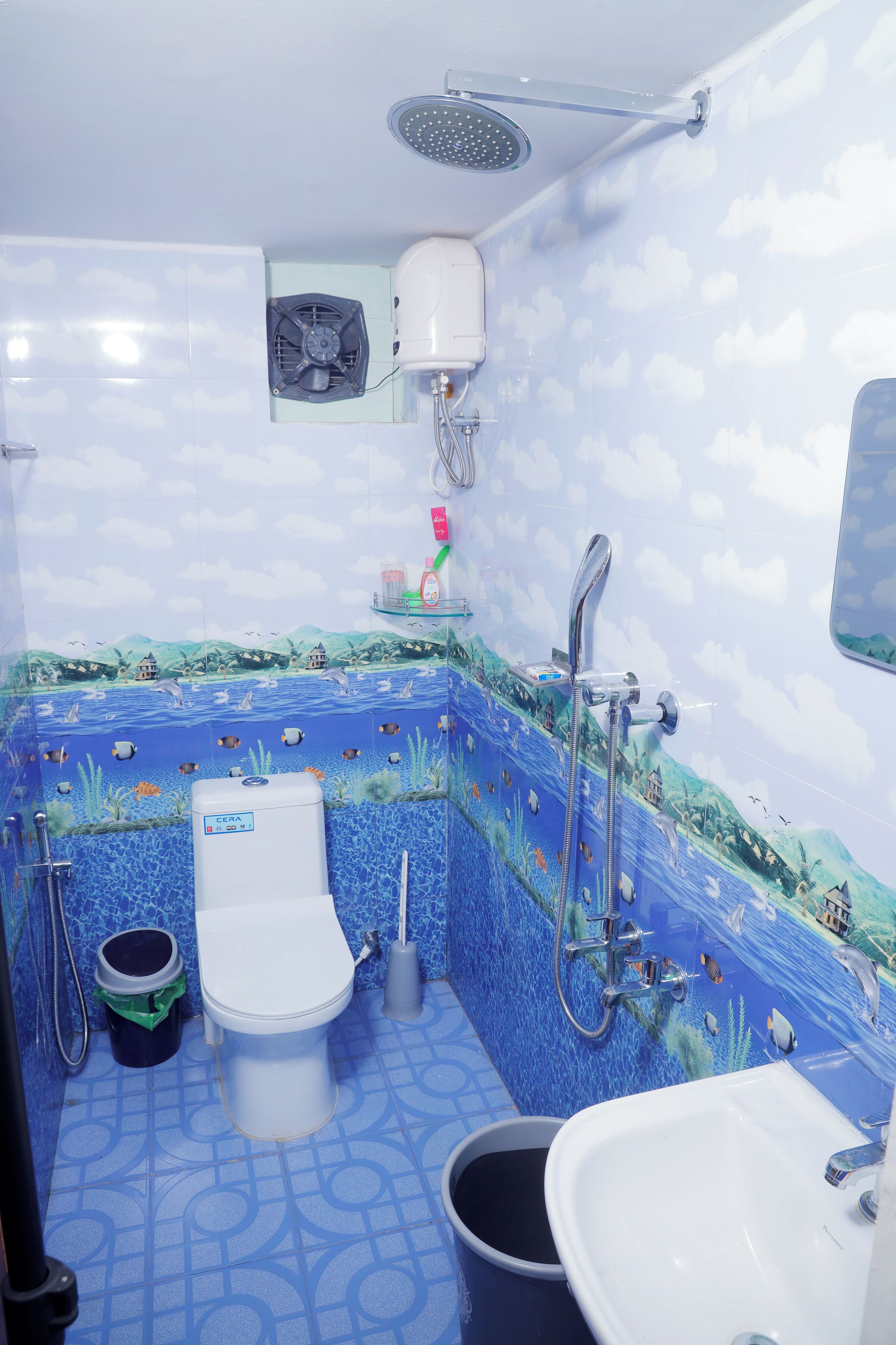 Ein Badezimmer mit Fliesen im blauen Meer-Design, einer Toilette, einem Waschbecken und einer Dusche.