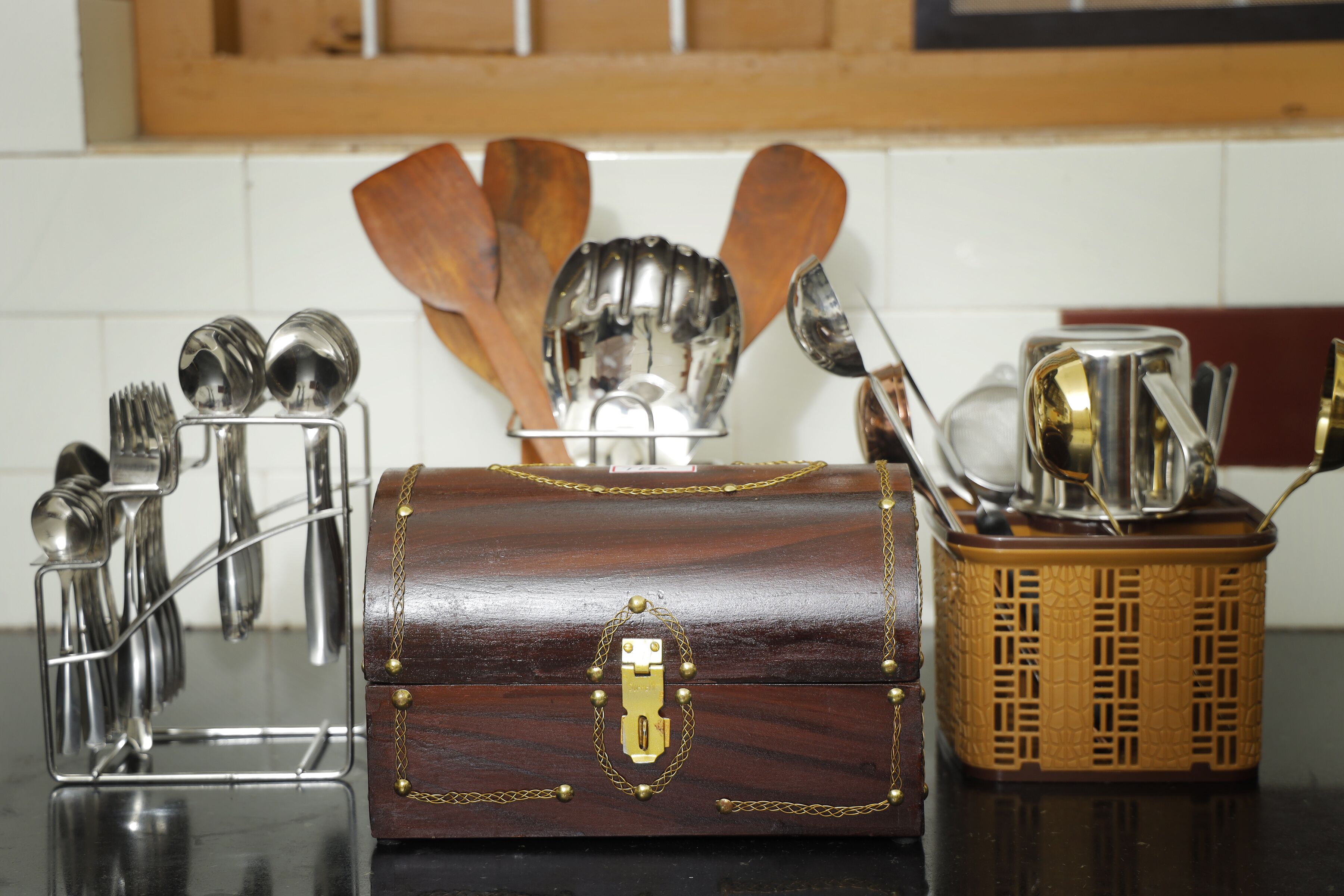 A kitchen counter with a wooden chest of drawers, a metal utensil holder, and a decorative container with spoons.
