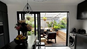 Une cuisine moderne dotée d’un grand îlot central, d’un coin repas avec une table et des chaises, et offrant une vue sur un jardin grâce à une porte ouverte.