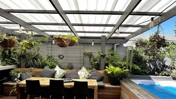 Un patio couvert avec une table et des chaises en bois, un banc et divers pots de plantes.