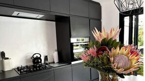 Une cuisine moderne équipée d’une cuisinière à gaz, d’une bouilloire et d’un vase orné de fleurs et de fruits.