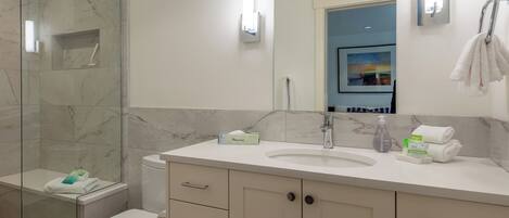 Un baño moderno con ducha de vidrio, lavamanos blanco y retrete.