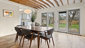 A dining area with a wooden table and chairs, a vase with plants, and a view of a backyard through glass doors. - 3BR Gem in Allandale (Austin)