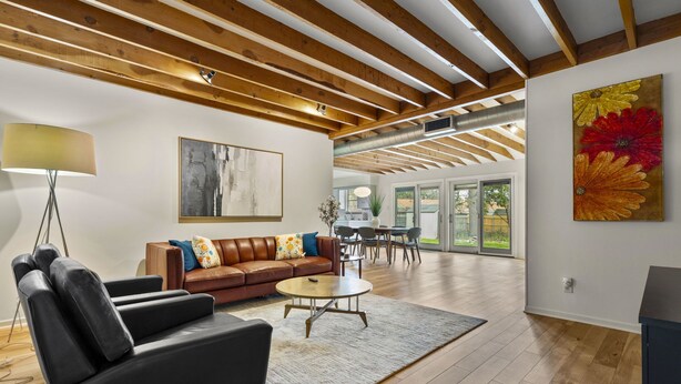 A spacious living room with a wooden ceiling, a leather sofa, a coffee table, and a large painting. - 3BR Gem in Allandale (Austin)