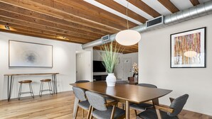 A modern dining area with a wooden table, grey upholstered chairs, and a white vase with plants. - 3BR Gem in Allandale (Austin)