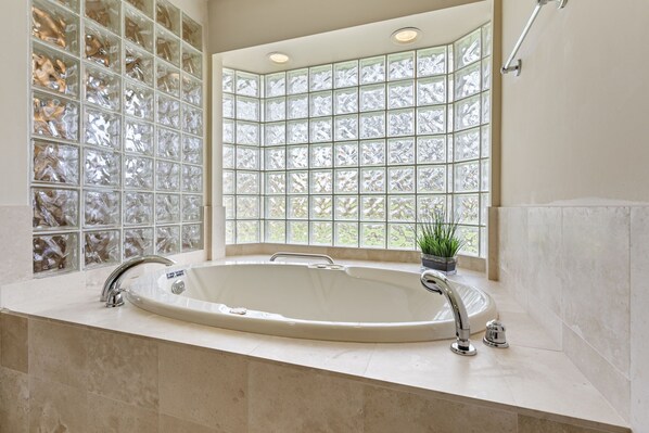 A bathroom with a large bathtub, a window with frosted glass panels, and a potted plant on the windowsill.