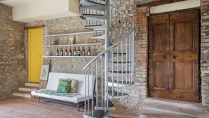 Un escalier en colimaçon dans une pièce rustique, avec un mur en pierre, une porte en bois et un canapé agrémenté d’un coussin vert.