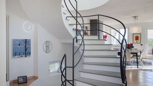 Una escalera moderna de diseño curvo, paredes blancas y un comedor con mesa y sillas.