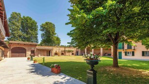 A courtyard with a brick building, a stone pathway, and a large tree. - Villa Fogliacchi - Five Bedroom Villa, Sleeps 10 (Fogliacchi)