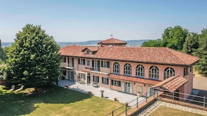 A large, two-story building with a red-tiled roof and arched windows, surrounded by lush greenery and a clear sky. - Villa Fogliacchi - Five Bedroom Villa, Sleeps 10 (Fogliacchi)