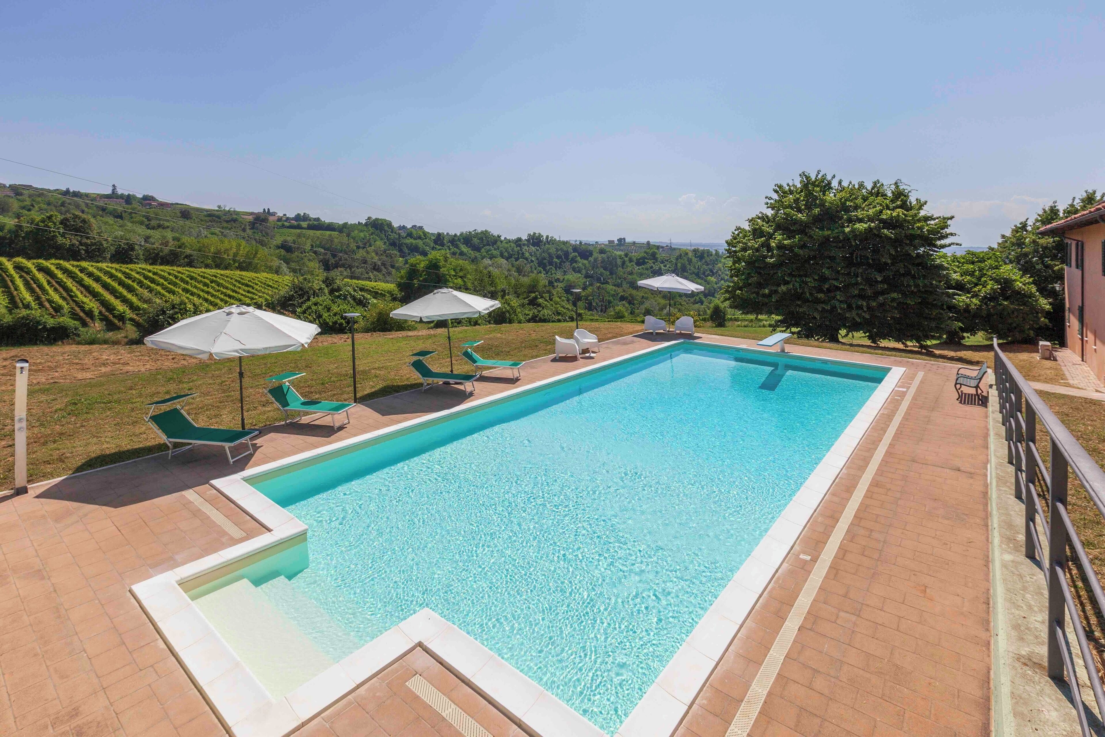 A rectangular swimming pool with a tiled deck, surrounded by lounge chairs and umbrellas.