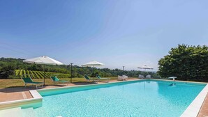 A rectangular swimming pool with clear blue water, surrounded by a tiled deck. There are lounge chairs and umbrellas along the poolside. - Villa Fogliacchi - Five Bedroom Villa, Sleeps 10 (Fogliacchi)