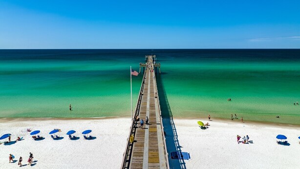 Ein Strand mit einer hölzernen Promenade, die sich ins Meer erstreckt, mit einer Flagge und einer Reihe von Strandsonnenschirmen.