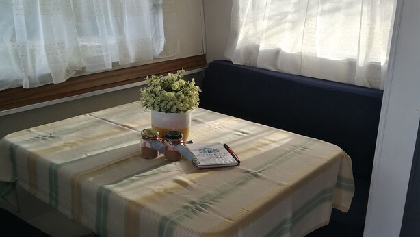 Un intérieur compact et bien éclairé, avec une table à manger dressée pour deux personnes, une petite plante en pot et un carnet.