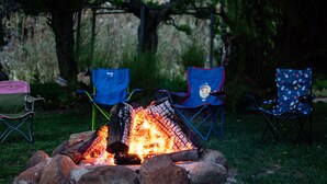 Un feu de camp entouré de trois chaises pliantes, installé dans une zone herbeuse avec des arbres en arrière-plan.