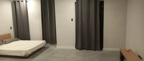 Un dormitorio con cama, ventilador de techo, cortinas grises y un banco de madera.