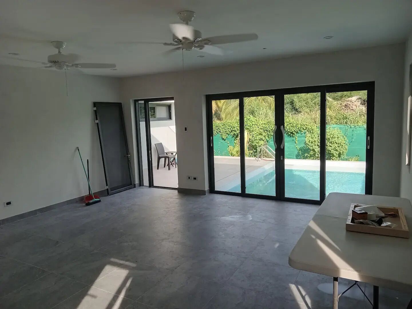 A spacious room with a large sliding glass door leading to a pool area, ceiling fans, and a table with items on it.