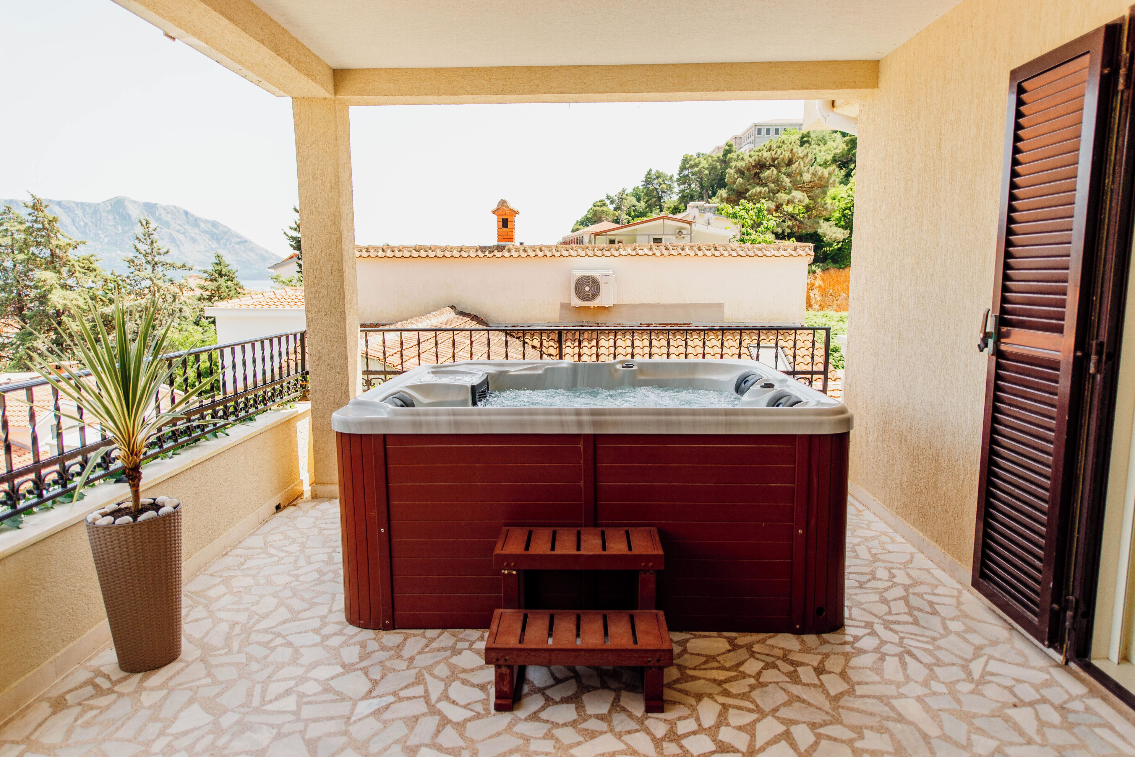 Een jacuzzi op een balkon, met uitzicht op bergen en een gebouw op de achtergrond.