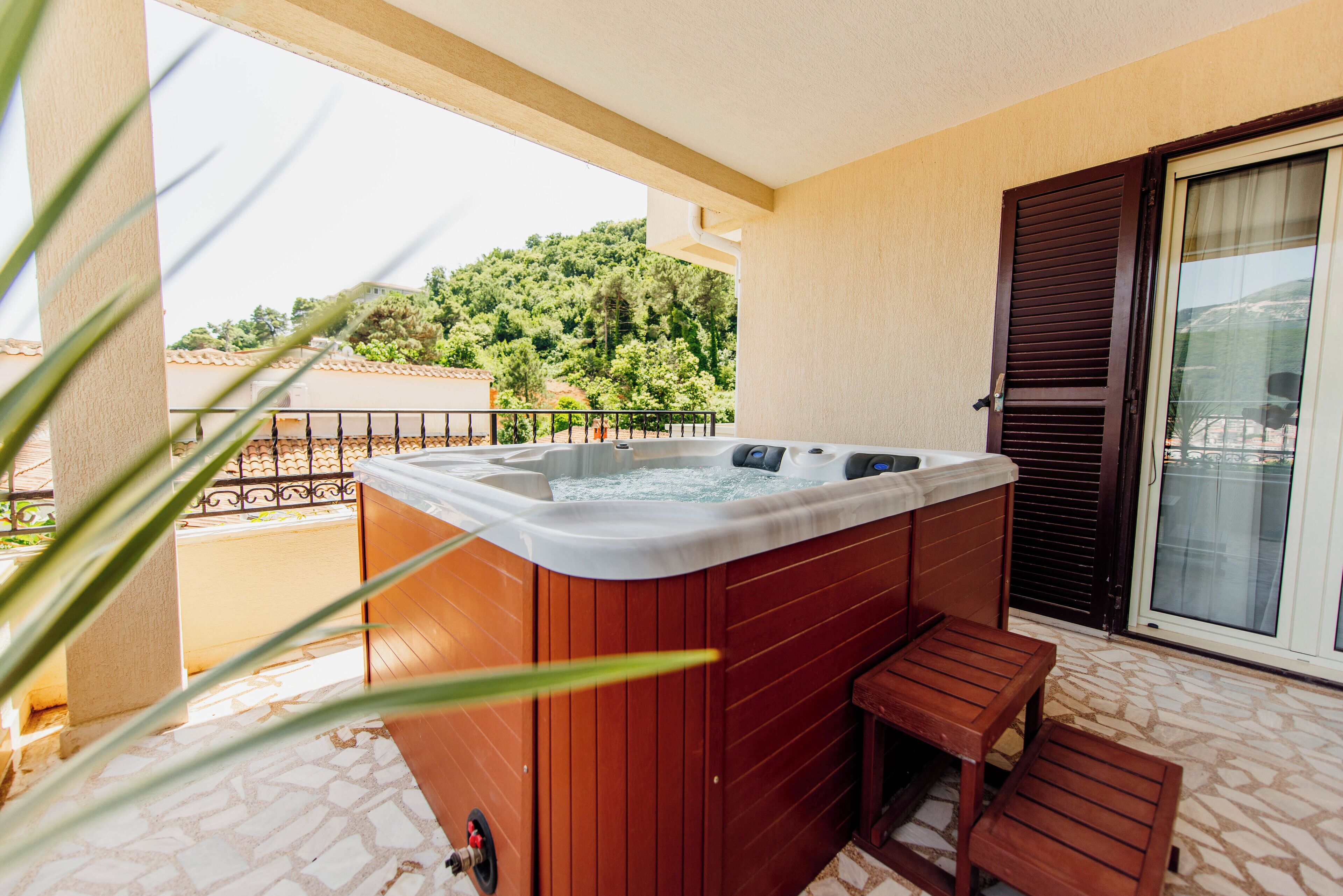 A hot tub on a balcony with a view of trees and a building in the background.