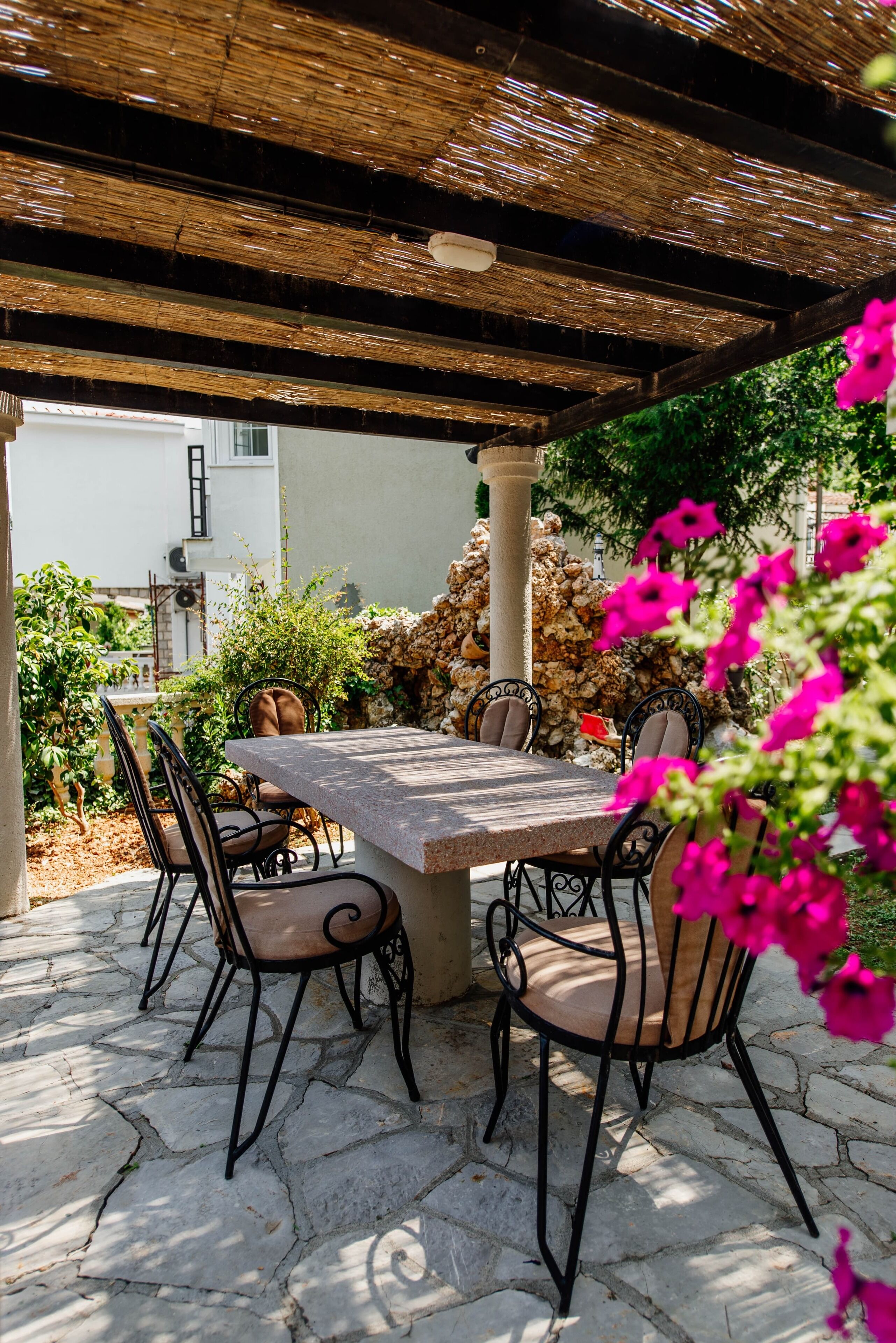 Une terrasse extérieure avec une table et des chaises en pierre, entourée de verdure et d’un mur de pierres.