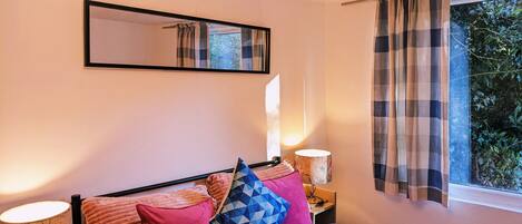 A bedroom with a bed, a bedside lamp, a mirror, and a window with curtains.
