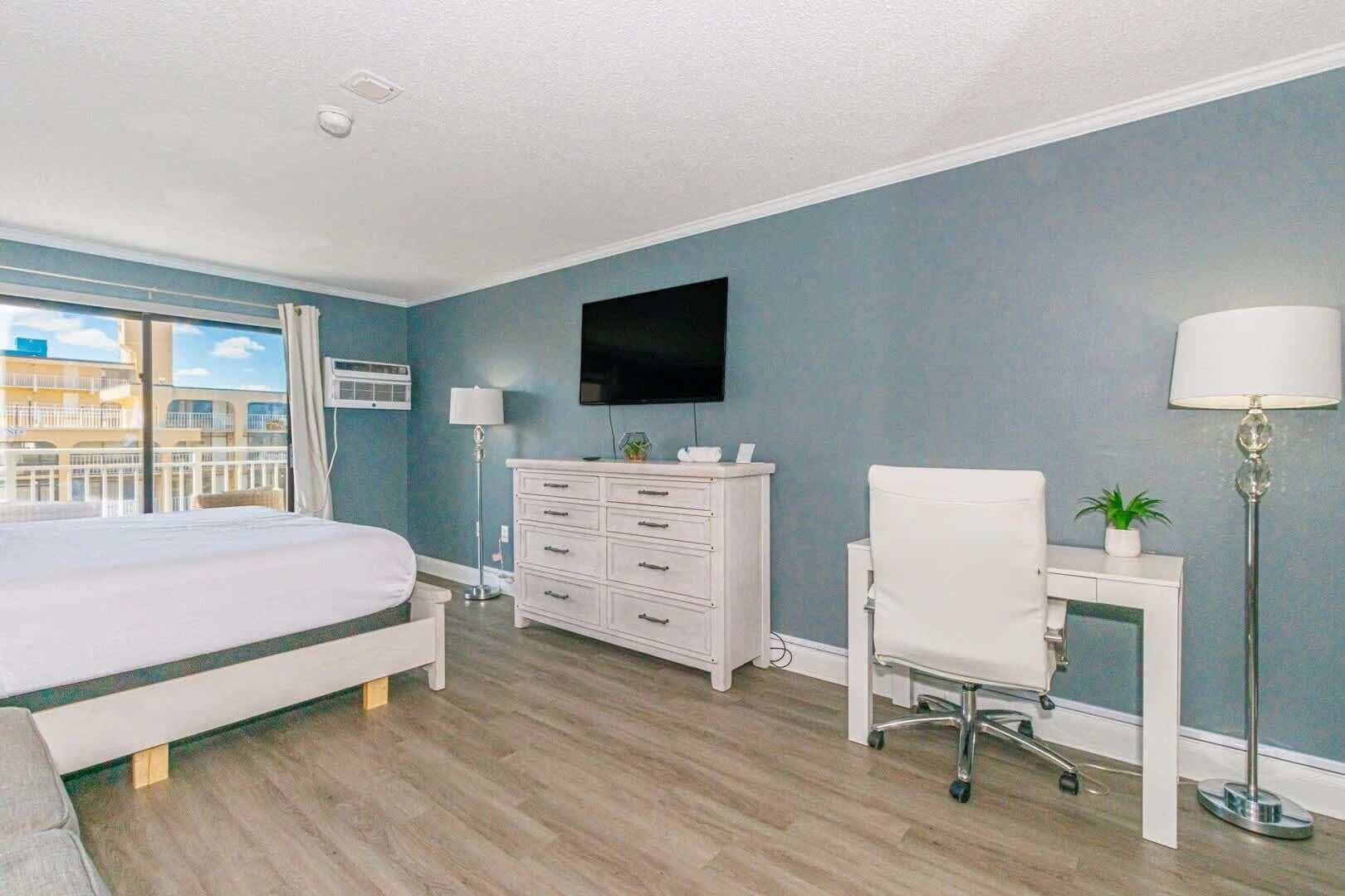 Une chambre d’hôtel équipée d’un lit, d’un bureau, d’une chaise, d’une télévision et d’une fenêtre donnant sur des immeubles.