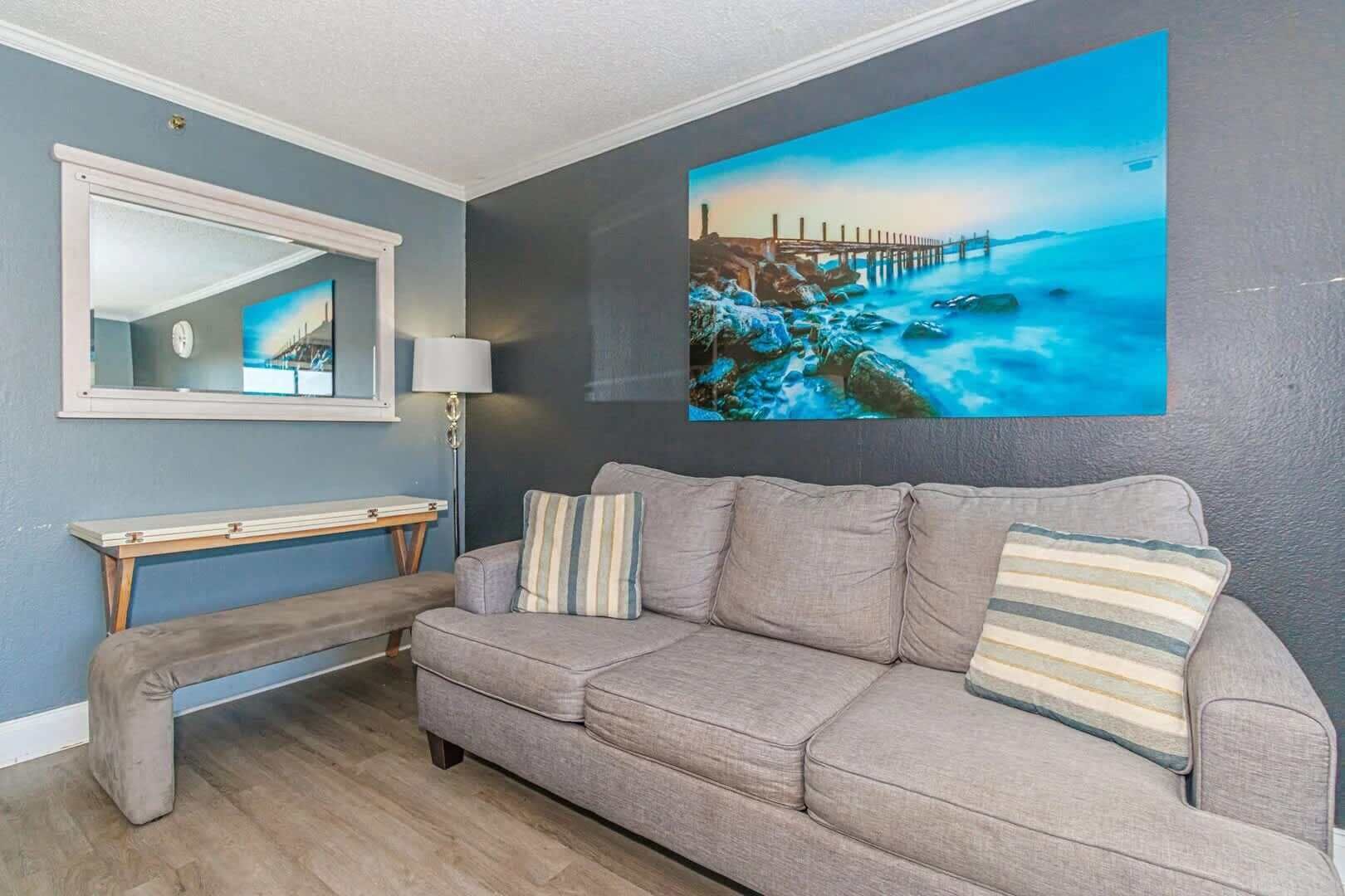 Una sala de estar con un sofá, un banco, una consola, una lámpara y un cuadro grande de una escena costera.