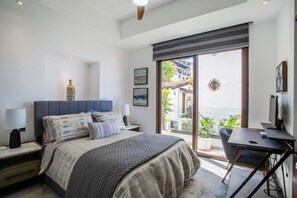 A bedroom with a bed, bedside tables, a desk, and a view of the outside.