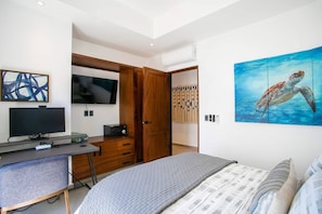A bedroom with a bed, a desk with a computer, a TV, and a painting of a sea turtle.