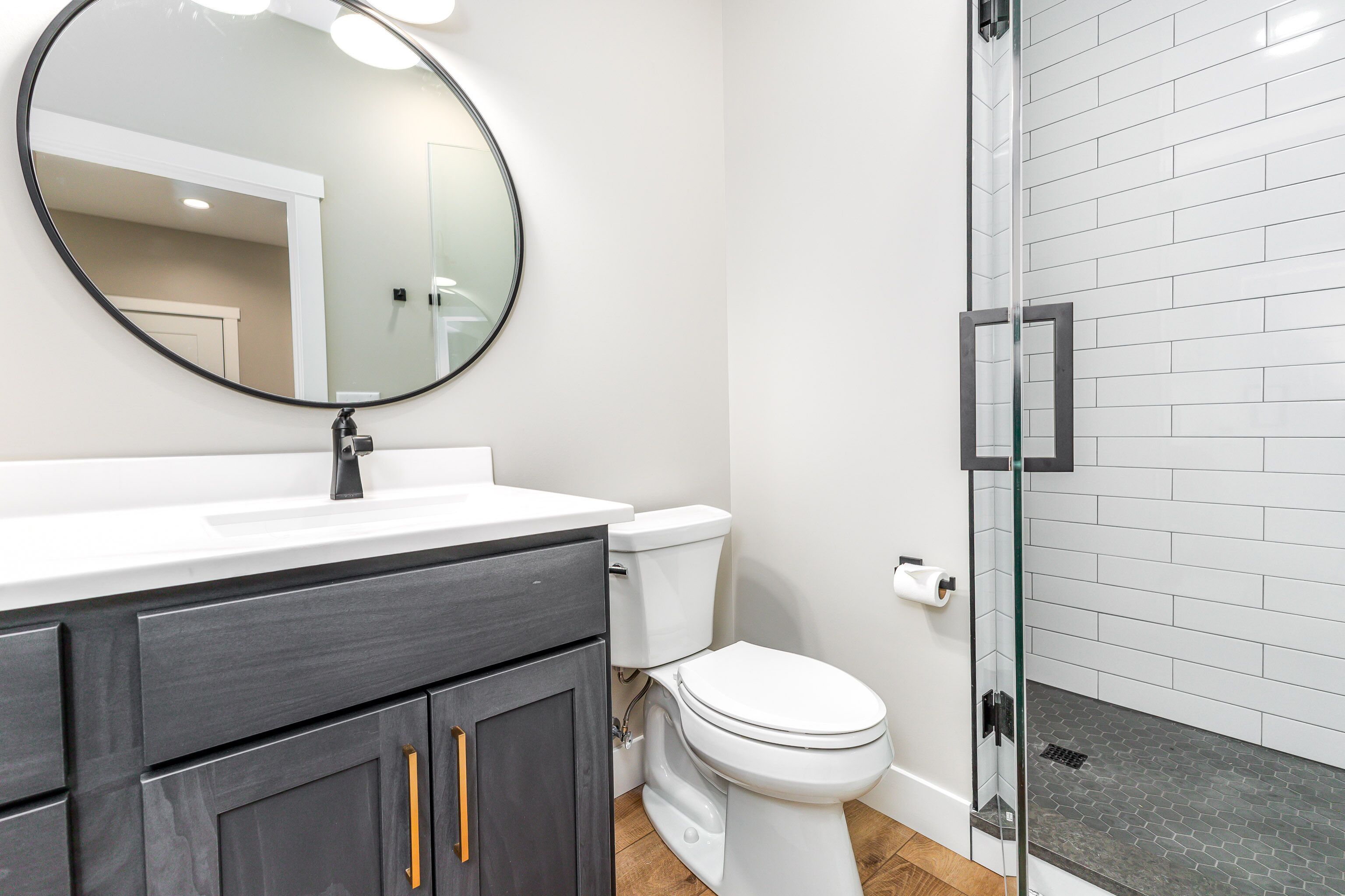 Een badkamer met een wit toilet, een ronde spiegel en een douchecabine van glas.