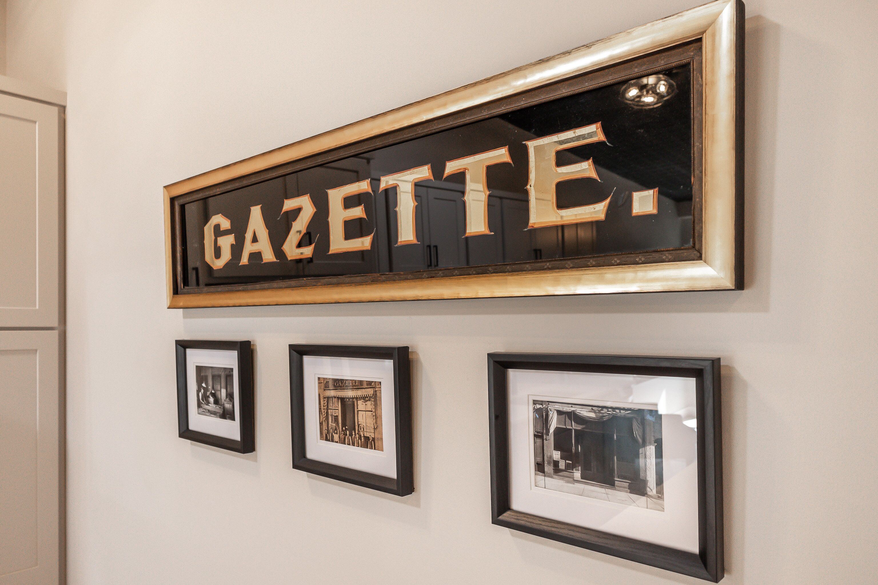 A wall with a framed sign reading "GAZETTE" and three framed photographs below it.
