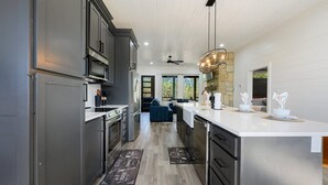 A modern kitchen with stainless steel appliances, a large island, and a view to a living area. - 54BD/3BTH Serenity Skyline Sleeps 14, Hot Tub and more! (Broken Bow)