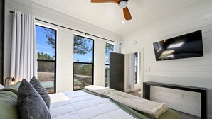 A modern bedroom with a large bed, a flat-screen TV, and a sliding glass door leading to an outdoor area. - 54BD/3BTH Serenity Skyline Sleeps 14, Hot Tub and more! (Broken Bow)