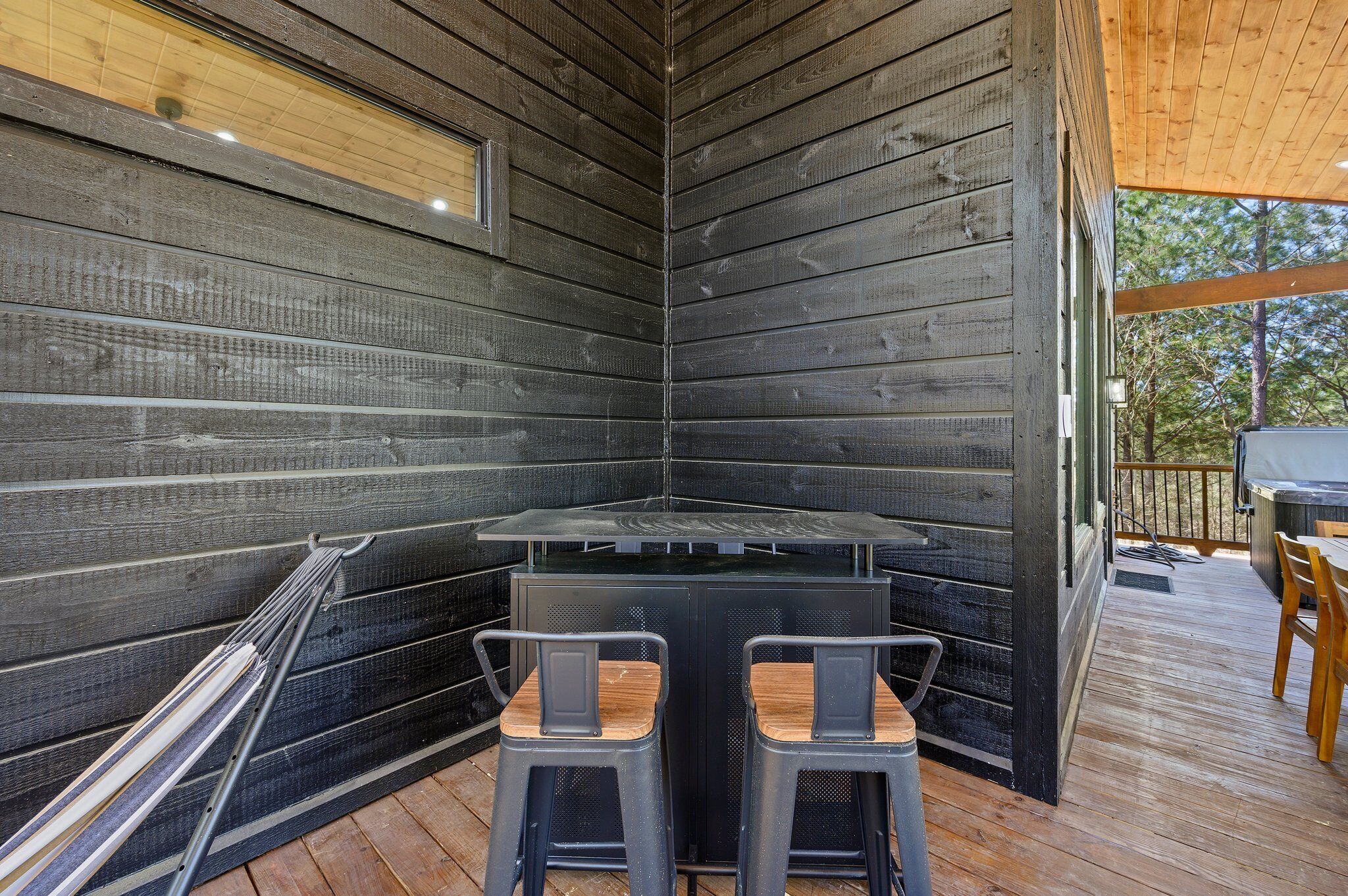 A corner of a wooden cabin with a metal table and two chairs, a window, and a deck area.