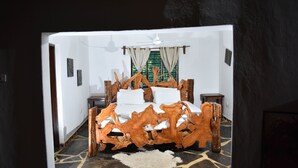 A bedroom with a unique wooden bed frame, a white bedspread, and a ceiling fan. - Spice of the coast  (Diani Beach)