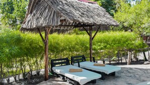 A thatched-roof structure with two beds under it, surrounded by greenery. - Spice of the coast  (Diani Beach)