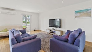 Una sala de estar moderna con un televisor de pantalla plana, dos sofás, una mesa de centro y un ventanal grande.