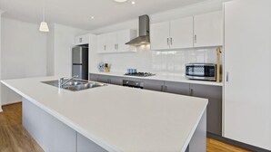 Una cocina moderna con armarios blancos, un lavamanos de acero inoxidable, un microondas y una estufa a gas.
