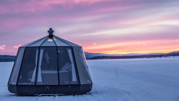 Une structure en forme de dôme géodésique se dresse sur un paysage gelé, avec un coucher de soleil en arrière-plan.