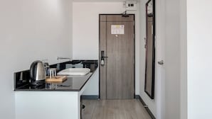 A compact kitchen with a sink, kettle, and coffee maker on a black countertop. - Area Place Hotel (Bangkok)