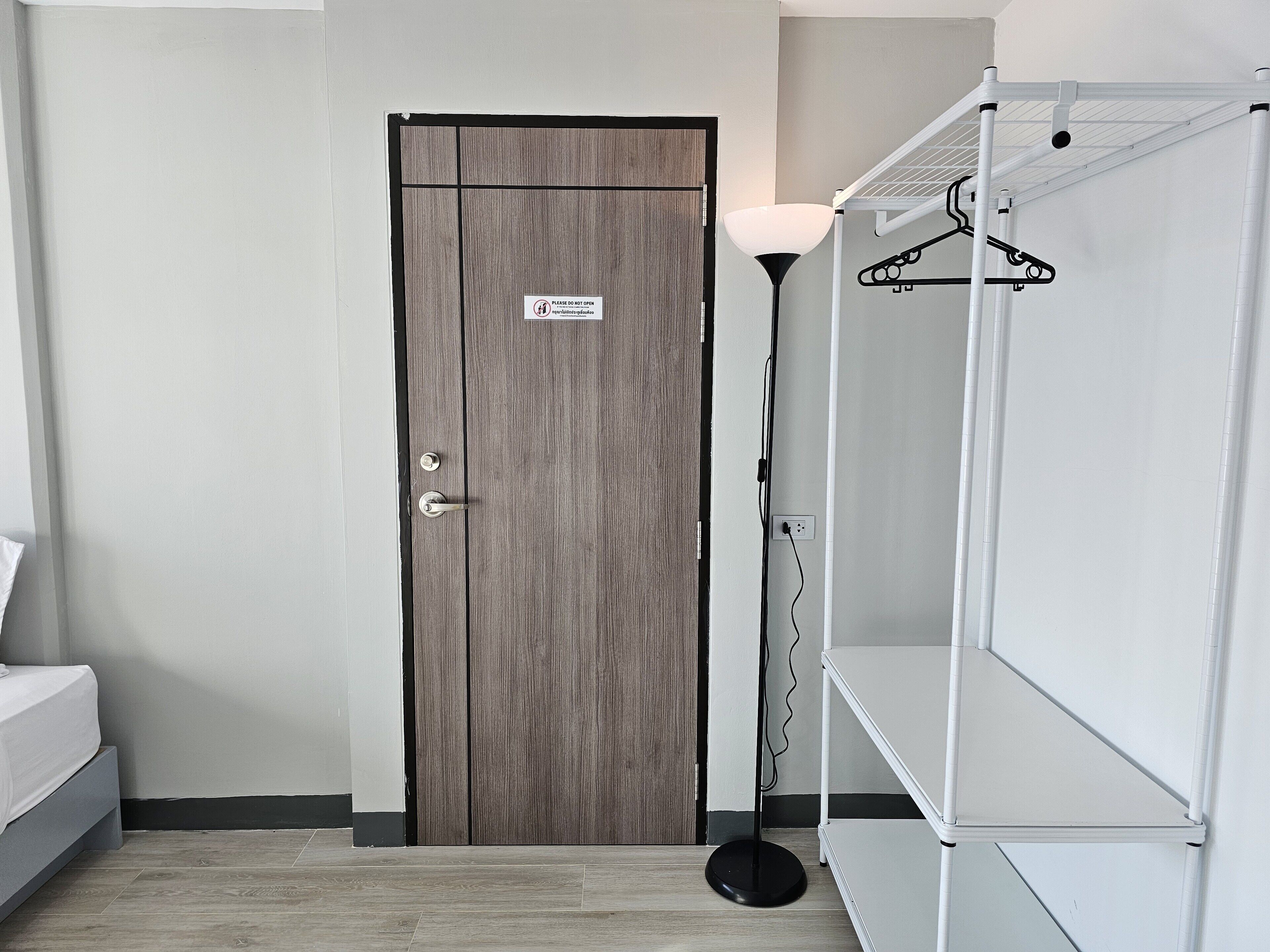 A room with a wooden door, a white closet with shelves, a floor lamp, and a bed.